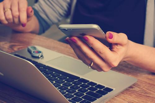 Woman looking at her iPhone while working on a macbook